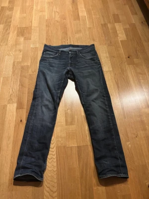 Mörkblå raka jeans från tiger of sweden - Säljer ett par mörkblå jeans från TOS med klassisk femficksdesign och raka ben. Jeansen har subtila slitningar och kontrastsömmar, samt en läderpatch bak i midjan. Perfekta till vardags och passar till det mesta. Materialet är slitstarkt jeans. Storleken är 32/32