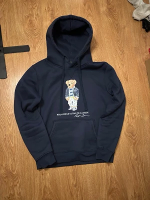 Polo bear hoodie - Säljer en marinblå stilig polo bear hoodie av Ralph Lauren. Den är i storlek M, skulle gissa på att den passar som bäst för de som är mellan 175-185.  Den har inga fläckar eller hål, den enda lilla defekten är att den är lite nopprig på något ställe. Jag skickar paketet inom 1 dag, hör av dig vid minsta fundering!