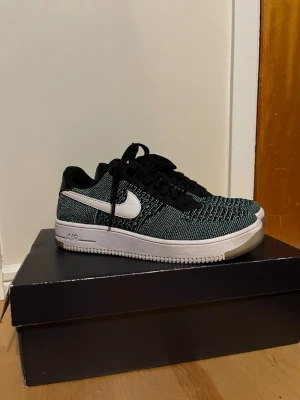 Nike Air Force 1 Flyknit Low svart/vit - Säljer ett par Nike Air Force 1 Flyknit Low i svart och vitt. soprena sneakers med stickad ovandel, vita swoosh-loggor och svart häl. Lätta och bekväma med klassisk vit sula och svarta skosnören. Perfekta för dig som vill ha en unik twist på klassikern.