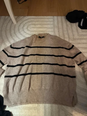 Beige randig stickad tröja Bik Bok  - Säljer en beige stickad tröja från H&M med svarta ränder. Tröjan har en relaxed passform, ribbade muddar och rund hals. Perfekt för dig som gillar en enkel men snygg look. Säljer då den inte kommer till användning storlek S.🖤🤎