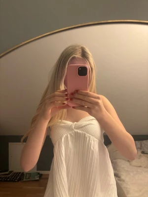 Vit axelbandslös bandeautopp - Säljer en superfin vit bandeautopp med twistad detalj framtill och plisserad nederdel. Toppen är axelbandslös och har en luftig, flowy känsla som passar perfekt till sommaren. Materialet känns mjukt och lätt mot huden.