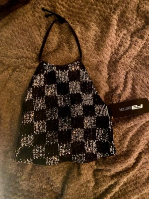 Svart och silver paljett halterneck topp - Säljer en snygg halterneck topp från FB Sister i svart och silver med rutigt mönster av paljetter. Toppen har knyt i nacken och är croppad.