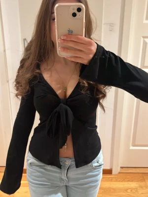 Svart långärmad knyttröja - Säljer en svart långärmad blus med djup v-ringning och stor knytning framtill. 