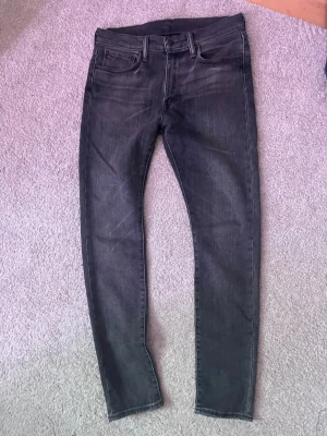 Levi's 519 mörkgrå jeans - Säljer ett par mörkgrå Levi's 519 jeans med klassisk femficksdesign och smal passform. Jeansen har en diskret tvättad look och är tillverkade i mjukt jeansmaterial. Perfekta för dig som gillar en clean och stilren vibe.