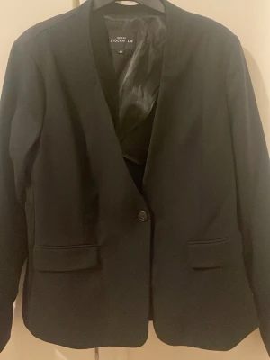 Svart kavaj från More by Stockh lm - Stilren svart kavaj från More by Stockh lm i storlek 44. Klassisk modell med en knapp framtill, två fickor med lock och slät insida i glansigt material. Perfekt för dig som vill ha en enkel och snygg look.