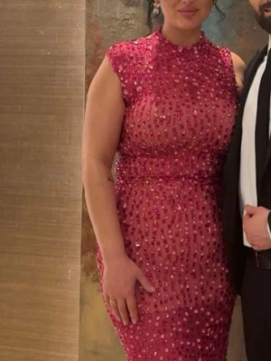 Glittrig rosa  paljettklänning - Säljer en rosa, glittrig klänning med massor av paljetter och stenar. Klänningen är figurnära, har hög hals och är ärmlös. Pris kan diskuteras 