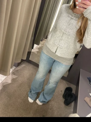 Grå kofta med rosettdetaljer - Superfin grå kofta med knappar och unika rosettdetaljer framtill. Mjuk och mysig känsla, perfekt för lager-på-lager. Rund halsringning och ribbade muddar vid ärmslut och nederkant. Passar perfekt till jeans eller kjol.