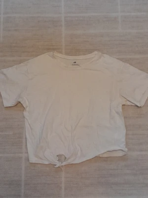 Vit t-shirt med knyt  - Vit t-shirt från H&M i mjuk bomull. Klassisk rund halsringning och korta ärmar. Nedtill finns en snygg knytning som ger en trendig touch. Perfekt till jeans eller shorts för en chill look. !!endast swish +frakt!!