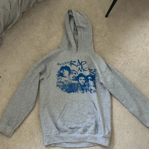 Grå hoodie Mount Rap More tryck - Grå hoodie med blått Mount Rap More-tryck framtill. Tillverkad i en mjuk blandning av bomull och polyester. 