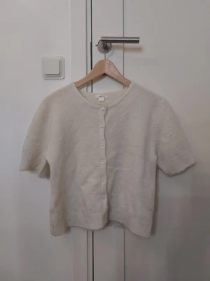 Vit kofta från Gina Tricot - mjuk och vit kofta från Gina Tricot med rund halsringning och korta ärmar. Koftan har knappar framtill och är stickad i ett fluffigt material som känns riktigt mysigt. Använd ca 4-5 gånger och är som ny❣️
