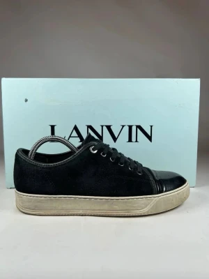 Svarta sneakers från Lanvin mocka/läder - PRISET GÅR ATT DISKUTERAS Säljer ett par svarta sneakers från Lanvin med ovandel i mocka och tåparti i blankt läder. Skorna har vita, lite smutsiga i sulan men det går att absolut att fixas och klassisk snörning. Perfekta för dig som gillar stilrena och exklusiva sneakers med en lyxig touch.