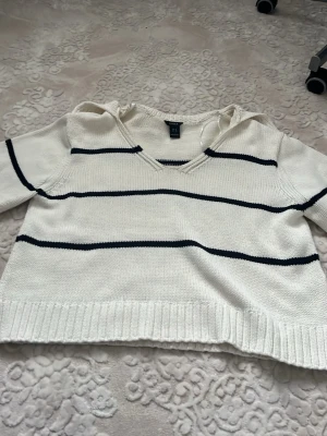 Vit och svart randig stickad tröja från Lindex - Vit stickad tröja från Lindex med svarta ränder. Tröjan har v-ringning och långa ärmar. Ribbstickade muddar vid ärmslut och nederkant som ger en extra fin effekt. Denna stickade tröja är verkligen jättetjock och håller dig jättevarm!! Perfekt för vintern.