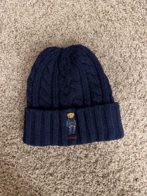  Ralph Lauren mössa - Säljer en stilren marinblå stickad mössa från Polo Ralph Lauren. Skön att ha nu i kylan och samtligt är den väldigt snygg. Endast testad. 