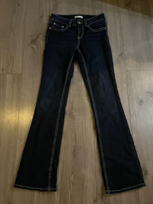 Mörkblå bootcut jeans med kontrastsömmar - Snygga mörkblå jeans med bootcut passform och tydliga vita kontrastsömmar. Klassisk femficksmodell med detaljerade bakfickor och låg midja. Perfekta för dig som vill ha ett par jeans som sticker ut lite extra. Använda en gång!!! Pris går att diskutera😊