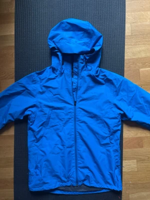 Blue Everest Windbreaker Size S - Säljer en blå vindjacka från Everest i storlek S. Jackan har huva med dragsko, hel dragkedja framtill och två sidofickor. Tillverkad i lätt och tålig polyester, perfekt för blåsiga dagar. Enkel och stilren design som funkar till det mesta.