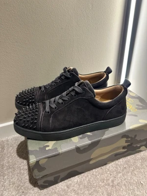 Christian Louboutin  - Svarta sneakers från Christian Louboutin med klassisk röd sula och coola nitar på tån. Skorna är gjorda i mocka och har snörning samt rund tå. Insidan är beige och sulan har Louboutin-loggan. Perfekt för dig som gillar edgy och lyxig stil. Hör av er vid funderingar🙌 bara skor ingen box eller dustbag medföljer, 8 spikar är borta men inget man märker då de sitter på kanterna. Mvh Melwin🙌
