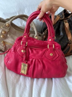 Röd rosa Q Classic Baby Groove väska - Så cool rosaröd handväska i äkta läder från Marc by Marc Jacobs. Den ikoniska modellen Q Classic Baby Groove! En populär och eftertraktad vintagemodell med gulddetaljer och dubbla handtag. Långa bandet finns. Så fint skick och en otroligt snygg vintage väska🤍  Mått: 34x18x12 cm (undersida) Kan hämtas hemma hos mig i Nacka eller skickas 🤍