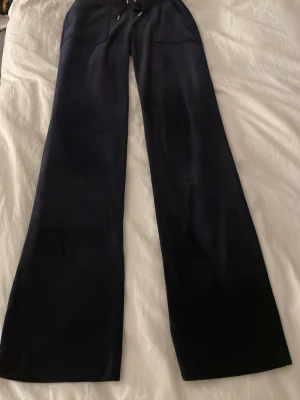 Svarta Juicy Couture mjukisbyxor XXS - Säljer ett par svarta mjukisbyxor från Juicy Couture i storlek XXS. Byxorna har breda ben, dragsko i midjan och fickor både fram och bak. Materialet är mjukt och glansigt, perfekt för en chill och snygg look.