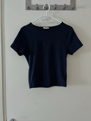 Mörkblå basic t-shirt Gina Tricot - En enkel och stilren mörkblå t-shirt från Gina Tricot, basically basics-kollektionen. Modellen har rund halsringning och korta ärmar. Perfekt till jeans eller kjol för en clean look.
