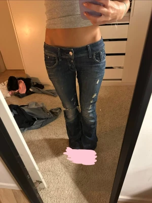 Lågmidjade blå bootcut jeans - säljer ett par mörkblå jeans som från början var skinny men som jag själv sytt om till bootcut. sömmen är ordentligt och snyggt sydd och ser bra ut i verkligheten. jeansen har låg/mellanmidja och lätt utsvängda ben med slitna detaljer och dragkedjor på bakfickorna för en extra edgy vibe. materialet är klassisk jeans i bomull och de har en snygg tvätt med ljusare partier på benen.