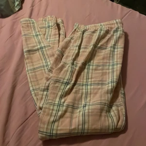 Rosa rutiga mjukisbyxor från 157 - Säljer ett par rosa mjukisbyxor från 157 i storlek M. Byxorna har ett rutigt mönster i rosa, vitt och mörkblått, med resår i midjan för extra komfort. Materialet är 100% bomull, vilket gör dem riktigt sköna att ha på sig. Perfekta för chill hemma eller mysiga kvällar.