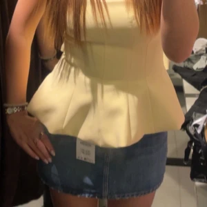 Gul axelbandslös bandeu top - Säljer en söt gul axelbandslös bandeu topp. Toppen har en figurnära passform upptill och volang nertill som ger en snygg siluett. 