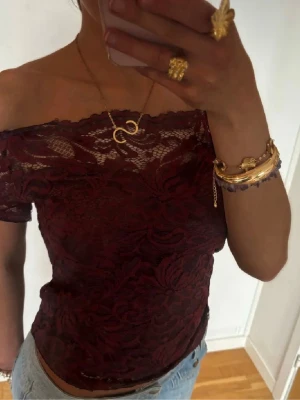 Bordeaux offshoulder spetsblus - Säljer en bordeauxfärgad offshoulder blus i spets med korta ärmar. Blusen har ett romantiskt mönster och sitter snyggt över axlarna. Perfekt för dig som vill ha en elegant och trendig topp med fina detaljer.