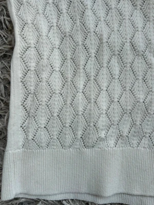 Vit stickad topp från H&M - Säljer en vit stickad topp från H&M med korta ärmar och ett snyggt hålmönster över hela plagget. Den har en liten liten rosa prick men det är knappast något som syns!!