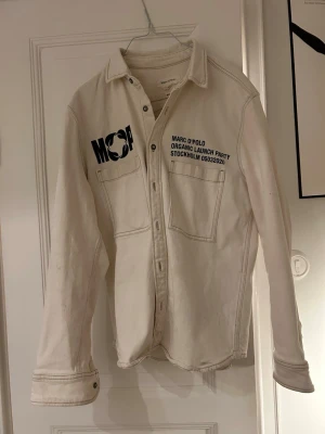 Vit overshirt från Marc O'Polo - Säljer en vit overshirt från Marc O'Polo med tryck på bröstet och två stora bröstfickor. Skjortan är tillverkad i ekologisk bomull med lite stretch och har knappar framtill. 