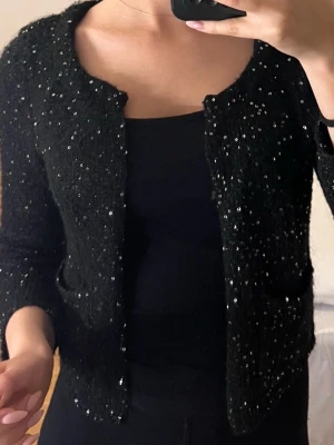 Svart paljettkofta från Divided - Svart kofta från Divided H&M som är täckt med glittriga paljetter. Koftan är stickad, har lång ärm och öppen front utan knappar. Den har kortare ärmar och passar bra till festliga sammanhang.