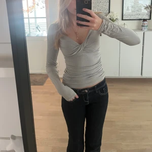 Ljusgrå omlottopp med v-ringning - Supersnygg ljusgrå topp med omlottdetalj och djup v-ringning. Långärmad och figurnära passform som framhäver midjan. Tunt och stretchigt material, perfekt att styla med jeans eller kjol.
