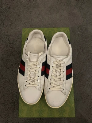 Gucci Ace skor  - Säljer dessa sjukt feta Gucci ace skorna som är i en ovanlig colorway, Röd och Mörkblå. Storlek 42 och box medföljer. Skorna är använda och har tecken på användning men har fortfarande mycket liv kvar i sig. Dessa är självklart äkta. Hör av dig vid minsta lilla fundering! 