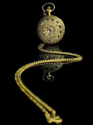 The Antique Timepiece - The Antique Timepiece är en elegant fickklocka i klassisk antik stil med vackert ornamenterat lock i guldfinish. Den detaljerade fronten ger ett tidlöst och exklusivt uttryck, medan den vita urtavlan med tydliga siffror gör klockan lätt att avläsa. Klockan levereras med matchande kedja och fungerar lika bra som stilfull accessoar som dekorativ detalj. Perfekt för dig som uppskattar vintage-känsla, klassisk design eller söker en unik present. Helt ny och i mycket fint skick.