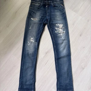 Blå Replay Grover jeans med slitningar - Säljer ett par blå Replay Grover jeans med snygga slitningar och tvättade detaljer. Klassisk femficksmodell med raka ben och normal passform. Perfekta för dig som gillar en avslappnad men stilren look.