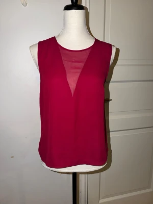 Vinröd ärmlös blus från Stockh LM - Vinröd blus från Stockh LM med transparent V-insats framtill. Ärmlös modell med rund halsringning och dragkedja bak. Tunt, lätt material som ger en luftig känsla och snyggt fall.         Mycket bra skick passar xs/s