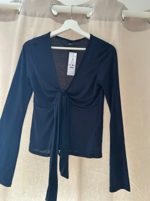 Mörkblå långärmad omlottopp Gina Tricot - Snygg mörkblå omlottopp från Gina Tricot i storlek M. Toppen har långa ärmar, djup v-ringning och knyt framtill som ger en cool och trendig look. Perfekt att styla med jeans eller kjol för en chill vibe.