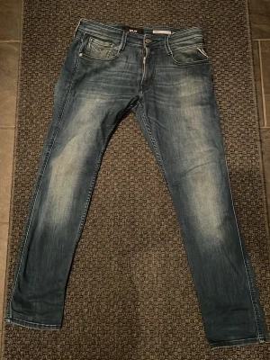 Replay blå slim jeans herr W31 L30 - Säljer ett par snygga Replay jeans i blå tvätt med slitningar och klassiska fem fickor. Modellen har smal passform och raka ben. Jeansen har dragkedja och knapp i midjan samt Replay-logga på bakfickan. Perfekta till en avslappnad streetstil.