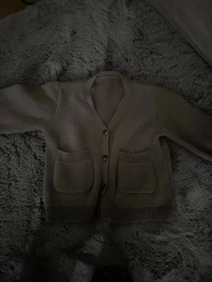 Beige stickad kofta / cardigan - Mysig beige stickad kofta med v-ringning och tre knappar framtill. Två stora fickor på framsidan och ribbade muddar vid ärmslut och nederkant. Köpt second hand så vet tyvärr inte märket, och skulle gissa på att storleken är S - M!!