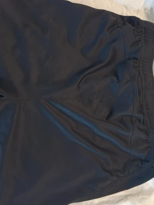 Svarta träningsshorts med tryck - Säljer ett par svarta träningsshorts med resår i midjan och tryck från STENA Recycling och IMAB på benen. Shortsen är gjorda i ett lätt och snabbtorkande syntetmaterial, perfekta för sport eller gym. Klassisk passform och stilren look.