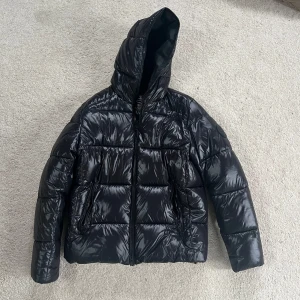 Svart pufferjacka Save The Duck storlek M - Säljer nu en svart save the duck jacka eftersom att jag behöver pengar. Jackan är i väldigt bra skick och bara använd en vinter varsamt. Dom ända ”defekterna” är att texten på insidan är lite ”skadad” och två väldigt små stygn på vänster arm som man knappt ser. Modellen på bilden är 187cm. Pris kan diskuteras.