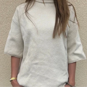 Vit polotröja med trekvartsärm - Säljer en vit polotröja med lös passform och trekvartsärm. Tröjan har en hög krage och är tillverkad i ett mjukt, frottéliknande material som känns skönt mot huden. Perfekt att styla med jeans eller kjol för en chill look.