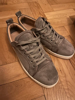 Grå mocka Christian Louboutin - Grå sneakers från Christian Louboutin i mjuk mocka med klassisk röd sula. Använda fåtal gånger. Pris kan diskuteras. 