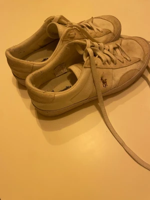 Vita sneakers Polo Ralph Lauren - Snygga vita sneakers från Polo Ralph Lauren med klassisk logga på sidan. Skorna har rund tå, platt sula och snörning. Ovandel i syntet och skinn, foder i textil och yttersula i gummi. Perfekt för dig som gillar stilren och sportig look.Bara använda några gånger.Villig att sänka pris