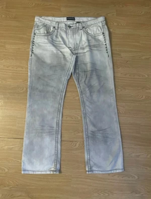 Kayden.K ljusa jeans med broderi - Säljer ett par ljusa jeans från Kayden.K med coola svarta broderier och detaljer på bakfickorna. Jeansen har raka ben, kontrastsömmar och är tillverkade i 100% bomull. Passar dig som gillar unik stil och snygga detaljer. Obs knapp saknas på ena bakfickan.