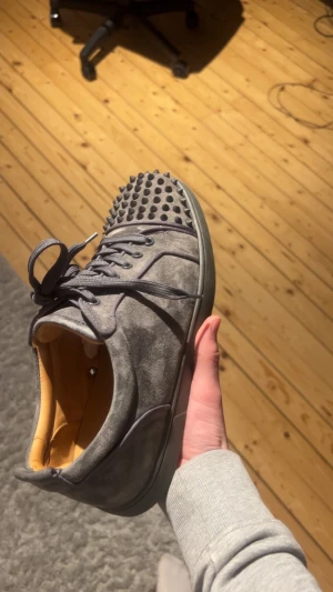 Grå Christian Louboutin sneakers med nitar - Säljer ett par grå sneakers från Christian Louboutin med coola nitar på tån och klassisk röd sula. Extra snören och nitar skickas med gratis men har tyvärr inte kvar sko lådan