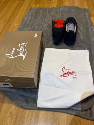Mörkblå sneakers från Christian Louboutin - Snygga mörkblå sneakers från Christian Louboutin med klassisk röd sula och rund tå. Skorna har snörning och är tillverkade i mocka med detaljer i textil. Insidan är beige och sulan har Louboutins signaturmönster. Box och dustbag medföljer. Pris kan diskuteras vid ett snabbt köp