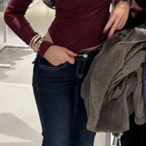 Vinröd oneshoulder långärmad topp - Säljer en vinröd långärmad topp med oneshoulder-design. Toppen är tight och croppad, vilket ger en snygg och modern siluett. Materialet är mjukt och stretchigt, troligen polyester, och färgen är djup vinröd. Perfekt för dig som gillar trendiga och stilrena plagg.