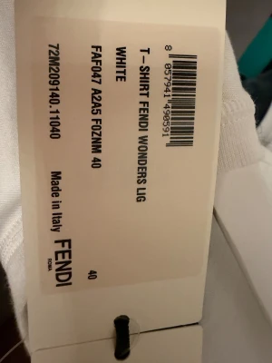 Vit Fendi t-shirt med orange tryck - Säljer en vit t-shirt från Fendi med coolt orange och rött ögonmotiv på bröstet. T-shirten har rund hals, korta ärmar och Fendi-logga i orange på ryggen. Tillverkad i mjuk bomull, perfekt för dig som gillar exklusiva märken och grafiska detaljer. Oanvänd! Köpt i milano 