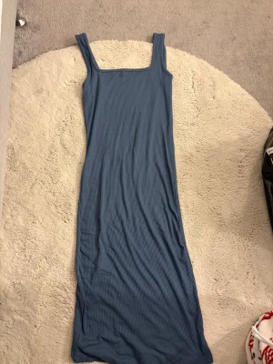 Blå ribbad långklänning 157 - Säljer en blå ribbad långklänning från 157 med breda axelband och fyrkantig ringning. Klänningen är figurnära och har en enkel, stilren design som passar perfekt till sommaren. Materialet är mjukt och stretchigt för en bekväm känsla.
