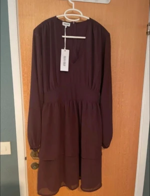 Vinröd klänning från Bubbleroom - Supersnygg vinröd klänning från Bubbleroom med v-ringning, långa transparenta ärmar och ett matchande bälte i midjan. Klänningen har ett flowigt fall och är tillverkad i ett lätt, skönt polyestertyg.